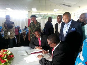 Peter signs the forms while running mate, Chilima, and EC chair, Mbendera, looks on